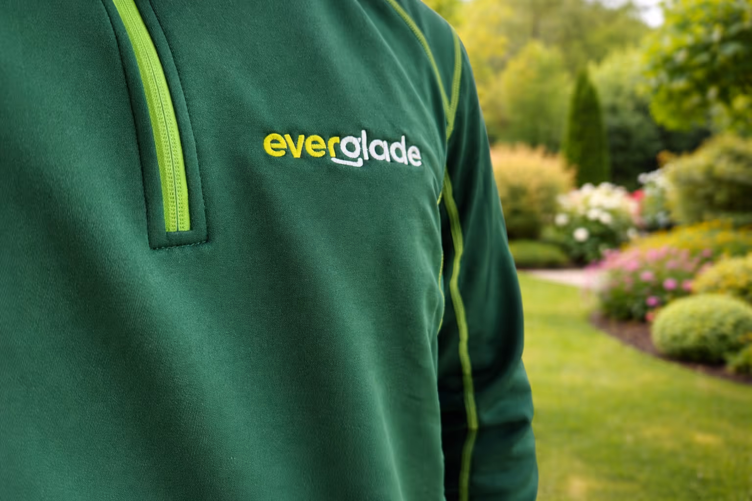 Arbeitskleidung der Everglade GmbH mit Firmenlogo vor einem gepflegten Garten