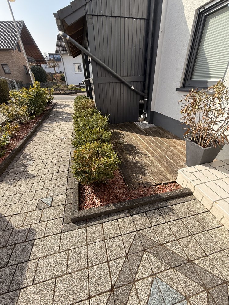 Vorher: Buchsbäume in Rindenmulch und eine verwitterte Holzterrasse neben dem Carport