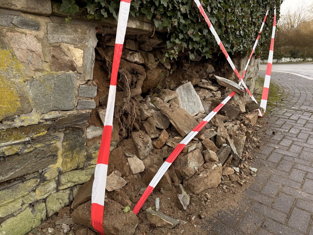 Nahaufnahme der eingestürzten Mauer mit Wurzeln und losen Steinen