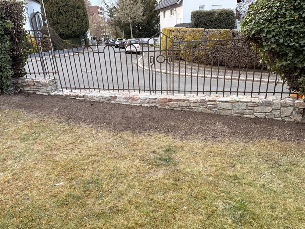 Neu aufgesetzte Natursteinmauer unter einem Metallzaun, von der Gartenseite gesehen