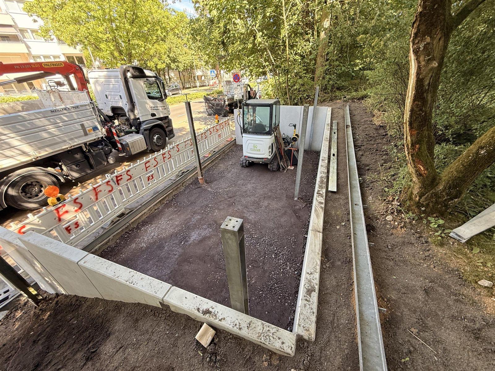 Minibagger in einer ausgehobenen und mit Winkelstützen eingefassten Baugrube in Wiesbaden, daneben ein Lkw mit Ladekran