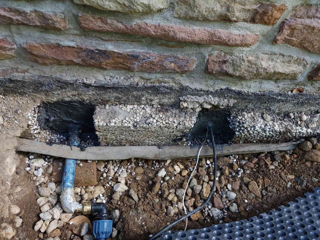 Hauswand mit zwei abgedichteten Kernbohrungen: links kommt die Wasserleitung heraus, rechts zwei Kabel