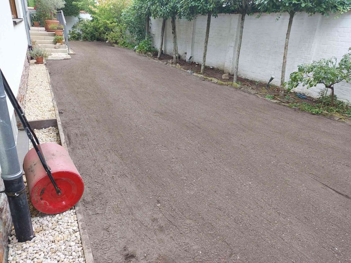 Neue Rasentragschicht, fein abgezogen, vorne eine rote Rasenwalze