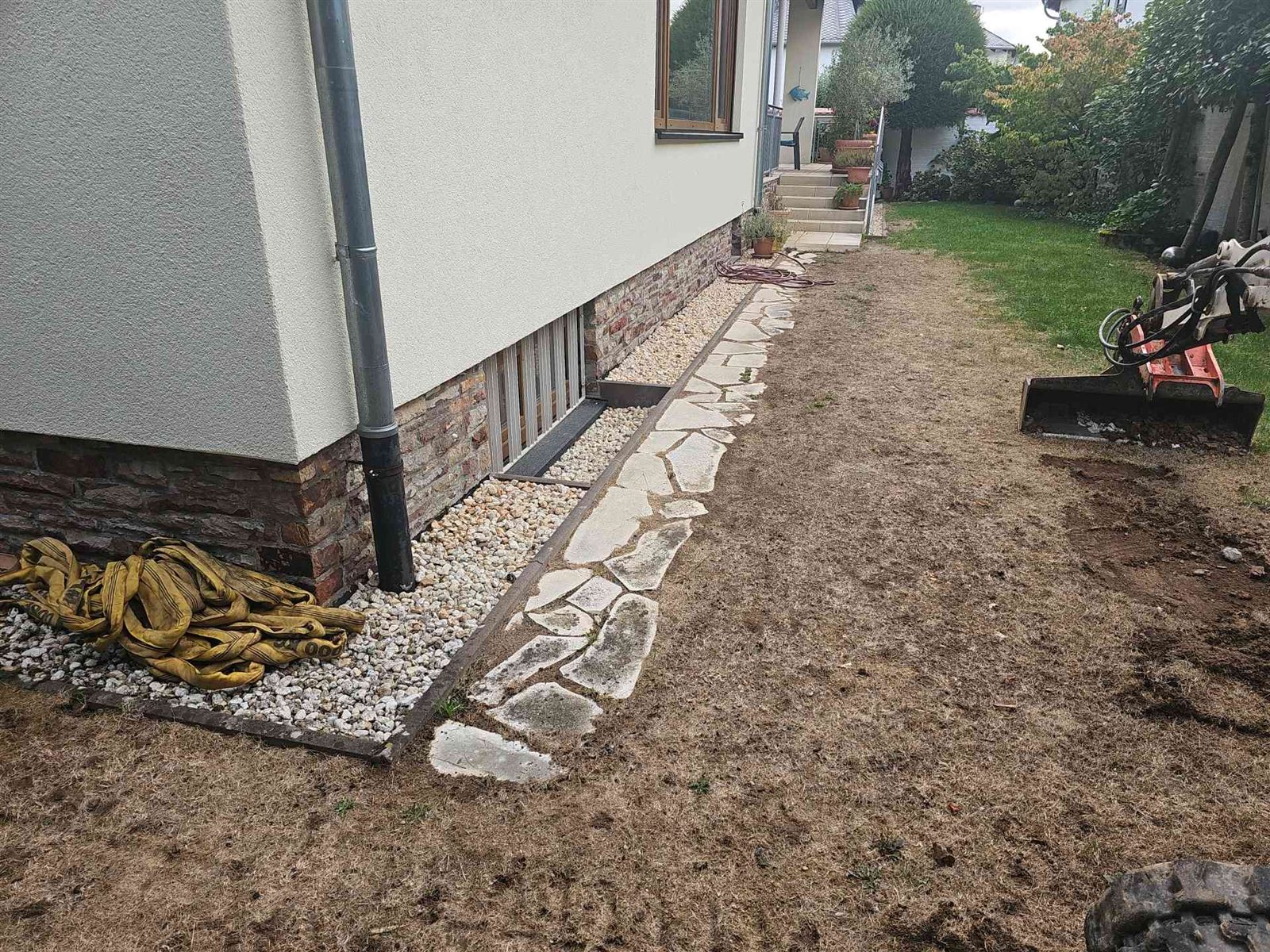 Vorher: vertrockneter, lückiger Rasen neben dem Haus, am Rand ein Weg aus Natursteinplatten