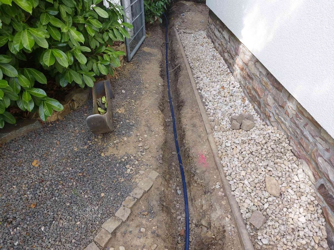 Die neue blaue Wasserleitung liegt in einem Graben entlang der Hauswand