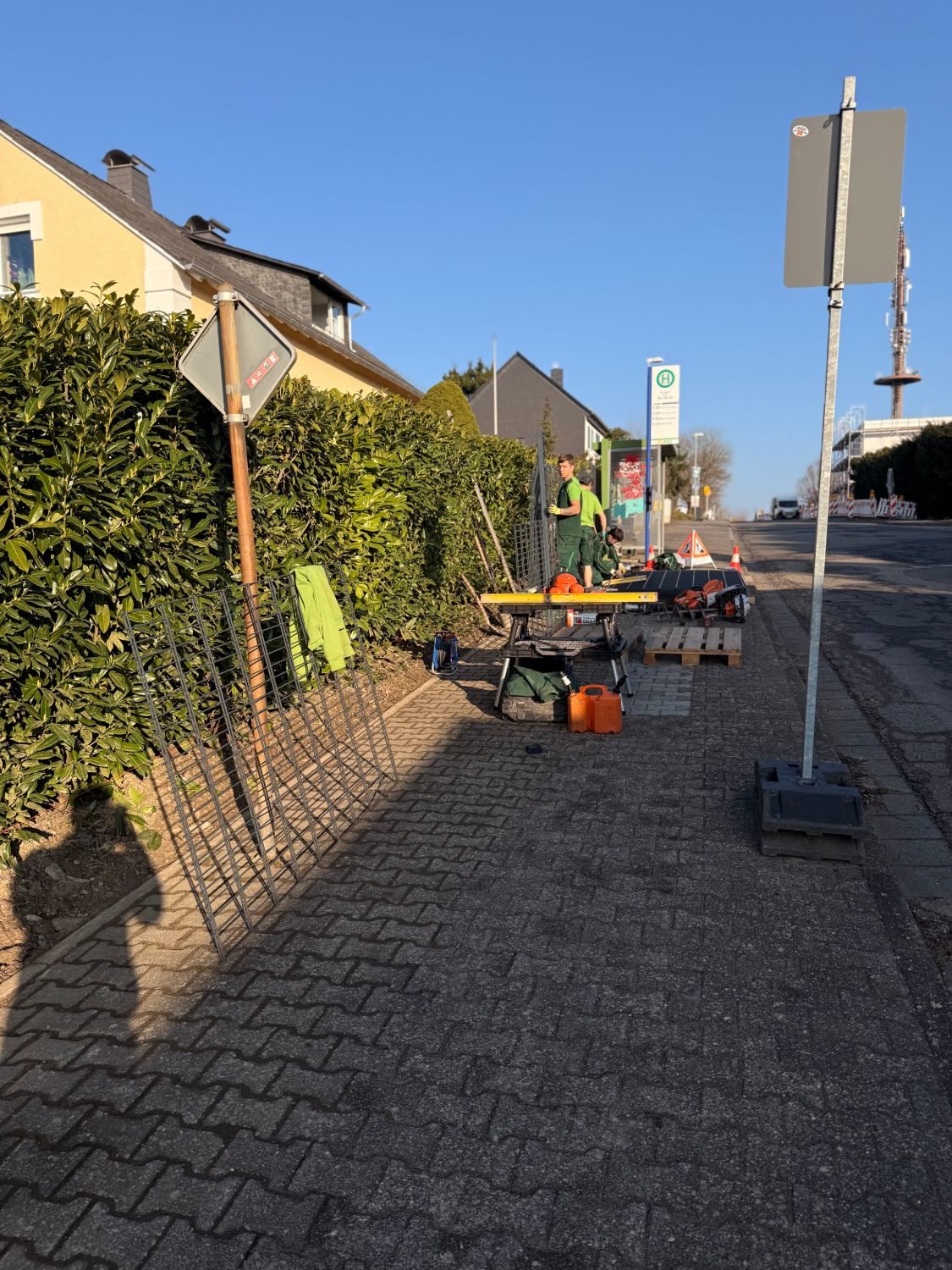 Baustelle am Gehweg mit Werkbank, Paletten, Matten und Warnschild, dahinter die Bushaltestelle