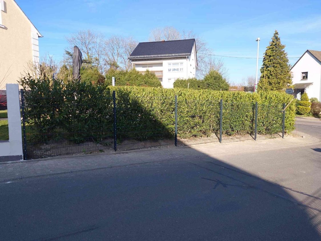Fertiger Zaun vor der Hecke an der Straßenecke, noch ohne Sichtschutz