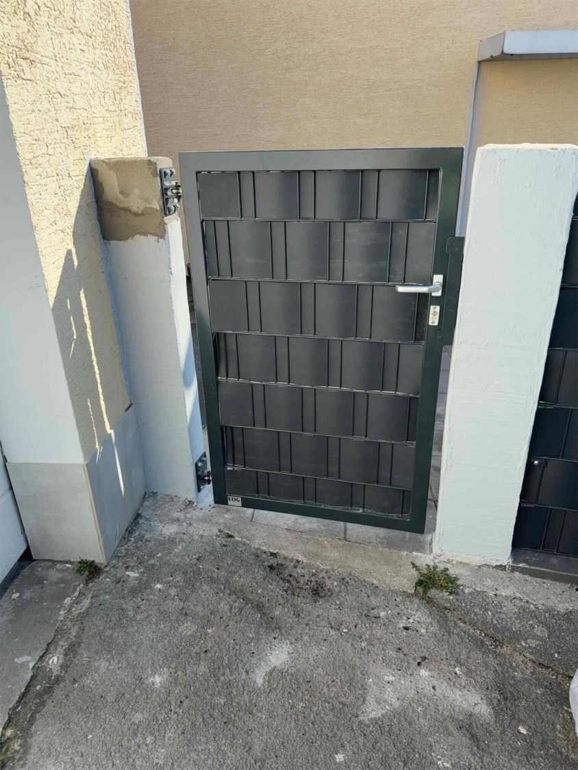 Einflügeliges Tor in Anthrazit mit eingefädeltem Sichtschutz zwischen zwei hellen Pfeilern
