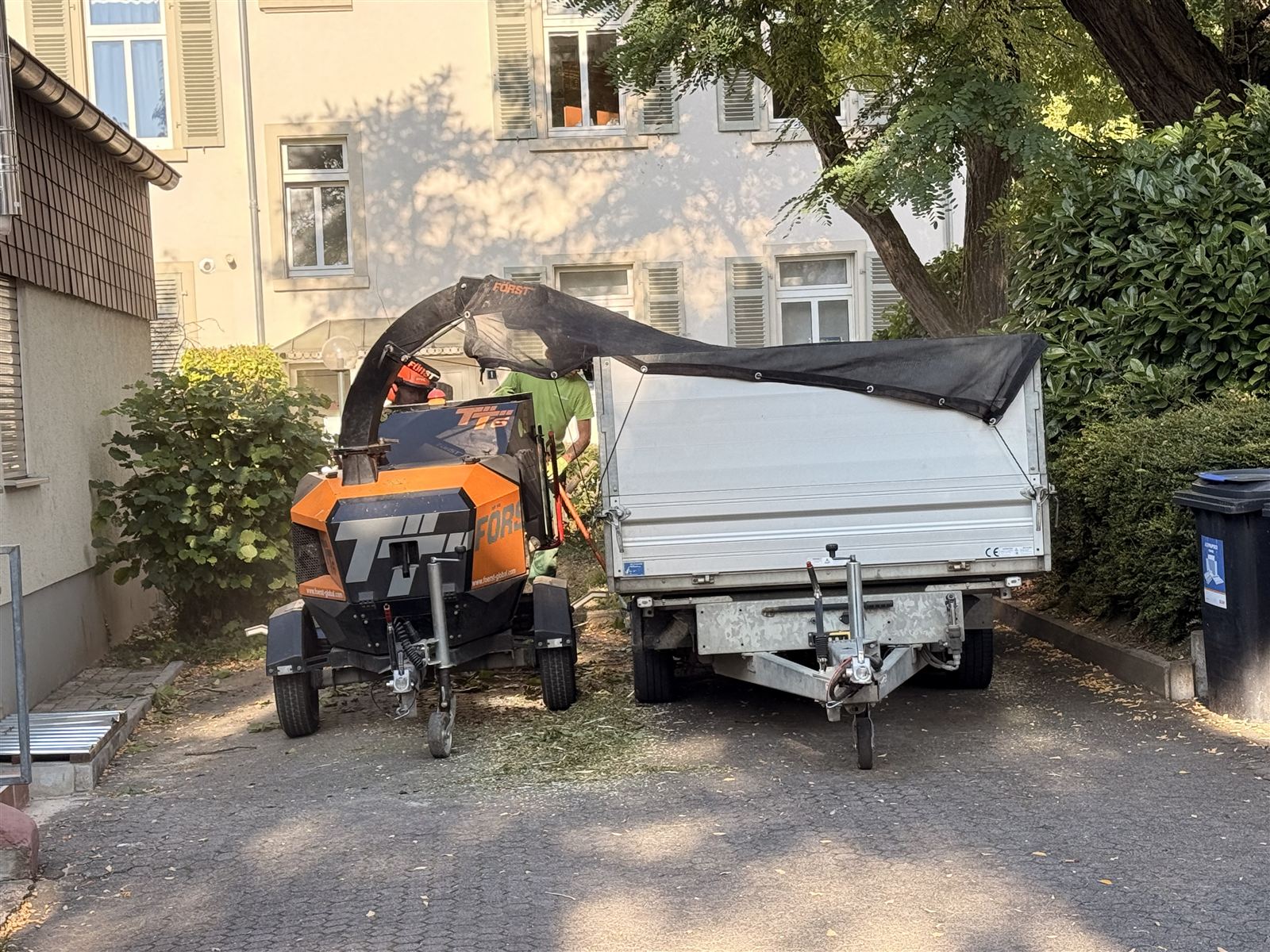 Häcksler und Anhänger mit Plane in der Hofeinfahrt einer Wohnanlage