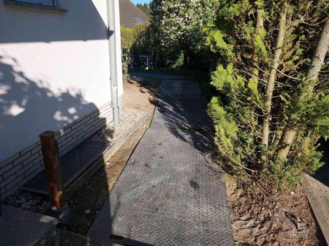 Lastverteilungsplatten liegen als Fahrweg über den Rasen entlang des Hauses