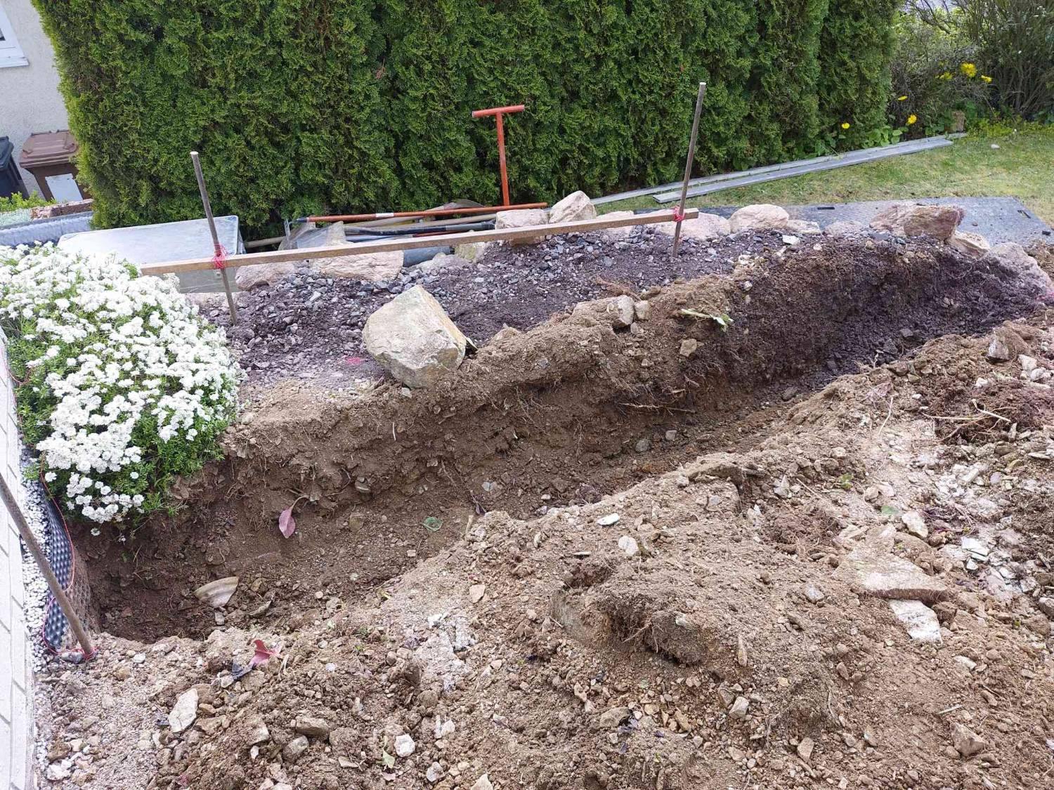 Graben für die Palisaden entlang der Hecke, darüber eine Schnur zwischen zwei Stäben