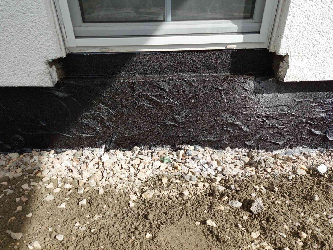 Schwarze Bitumen-Dickbeschichtung am Sockel unter der Terrassentür