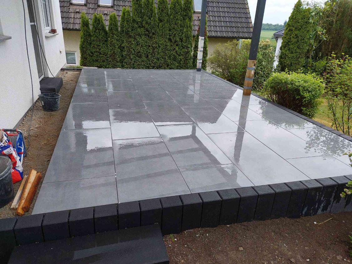 Fertig verlegte graue Keramikplatten im Drittelverband, eingefasst von Palisaden, vorne die Blockstufe
