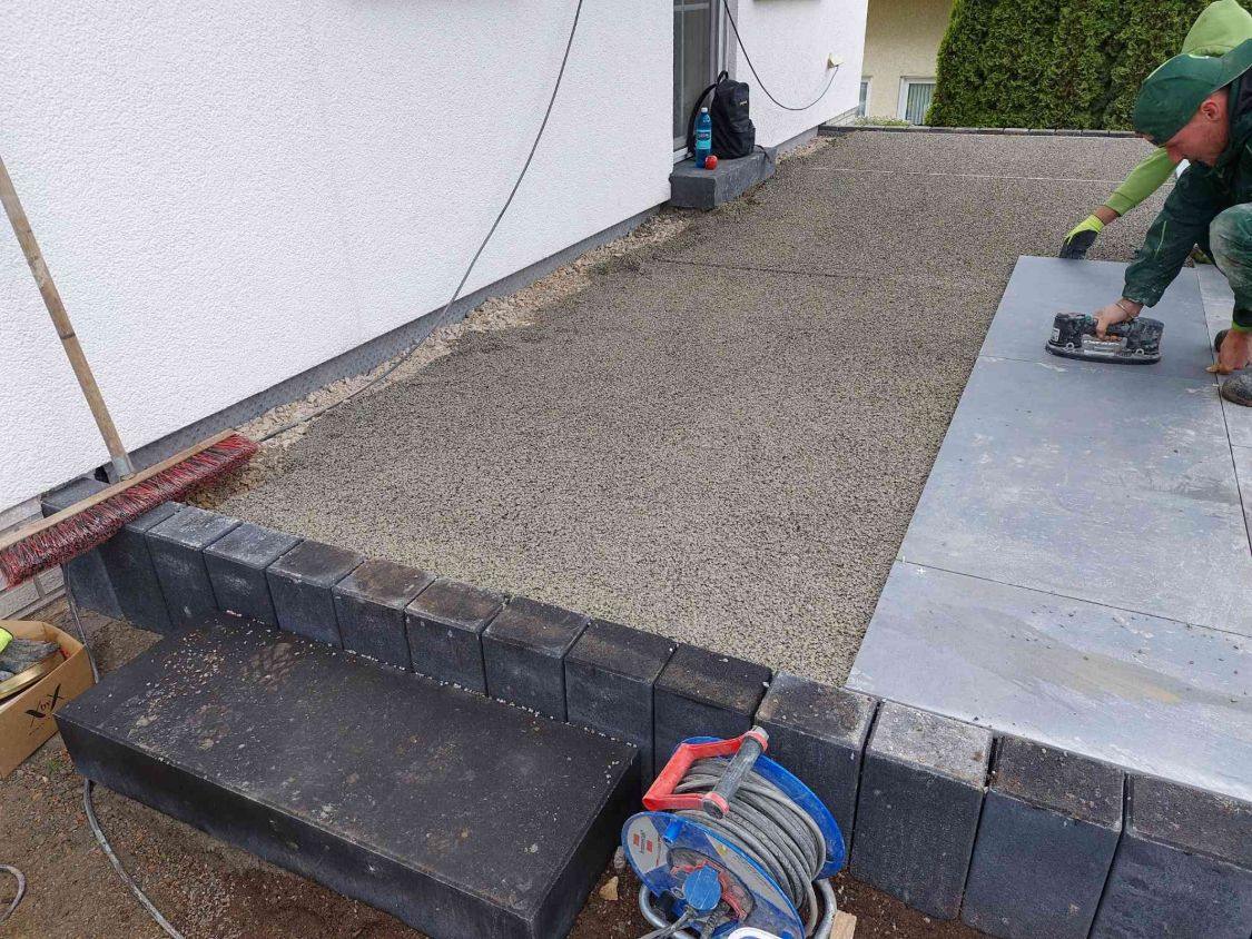 Mitarbeiter legt eine große Keramikplatte mit dem Saugheber auf das abgezogene Drainmörtelbett