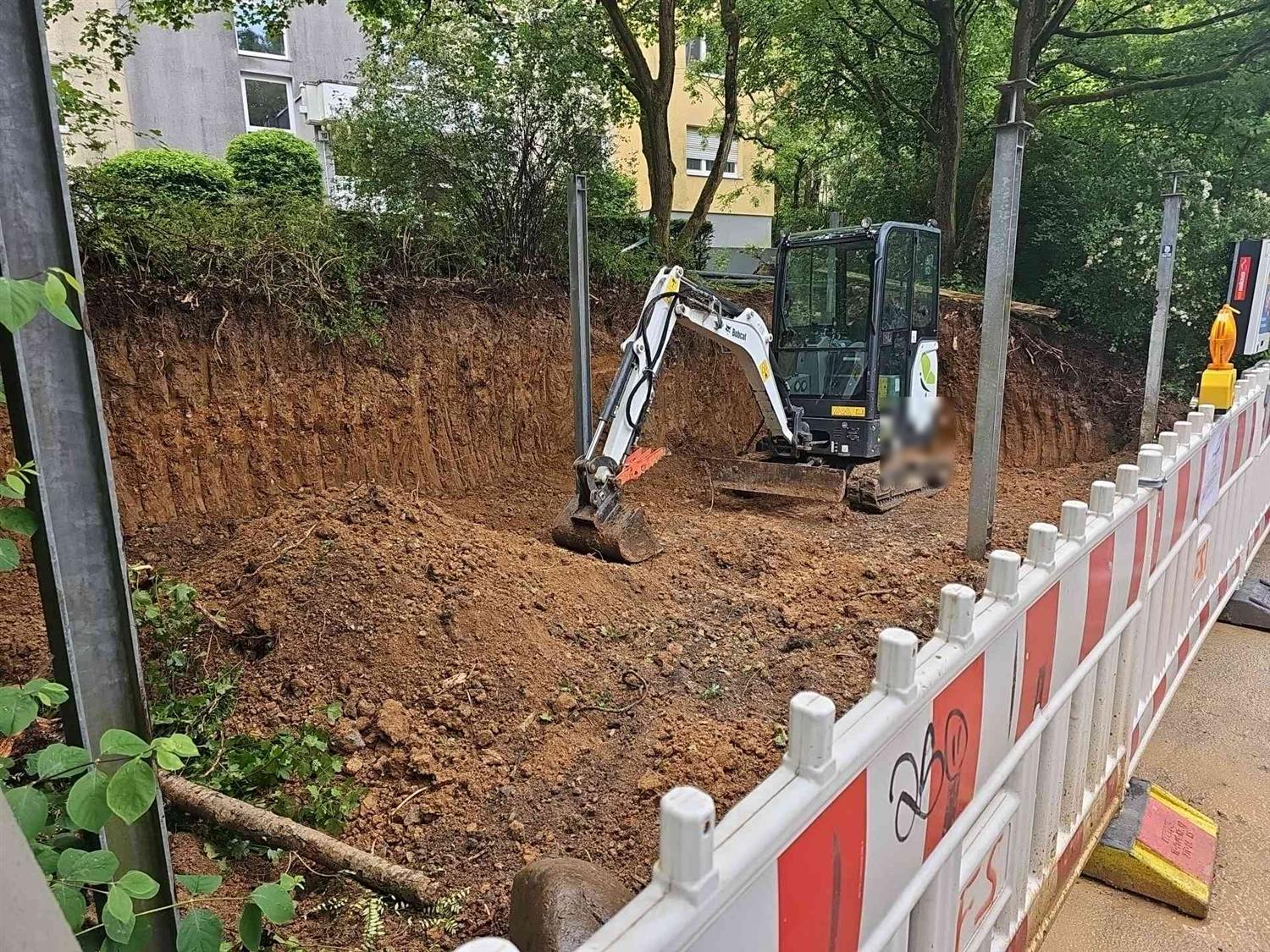Minibagger in der Grube, dahinter eine hohe, senkrecht abgegrabene Erdwand