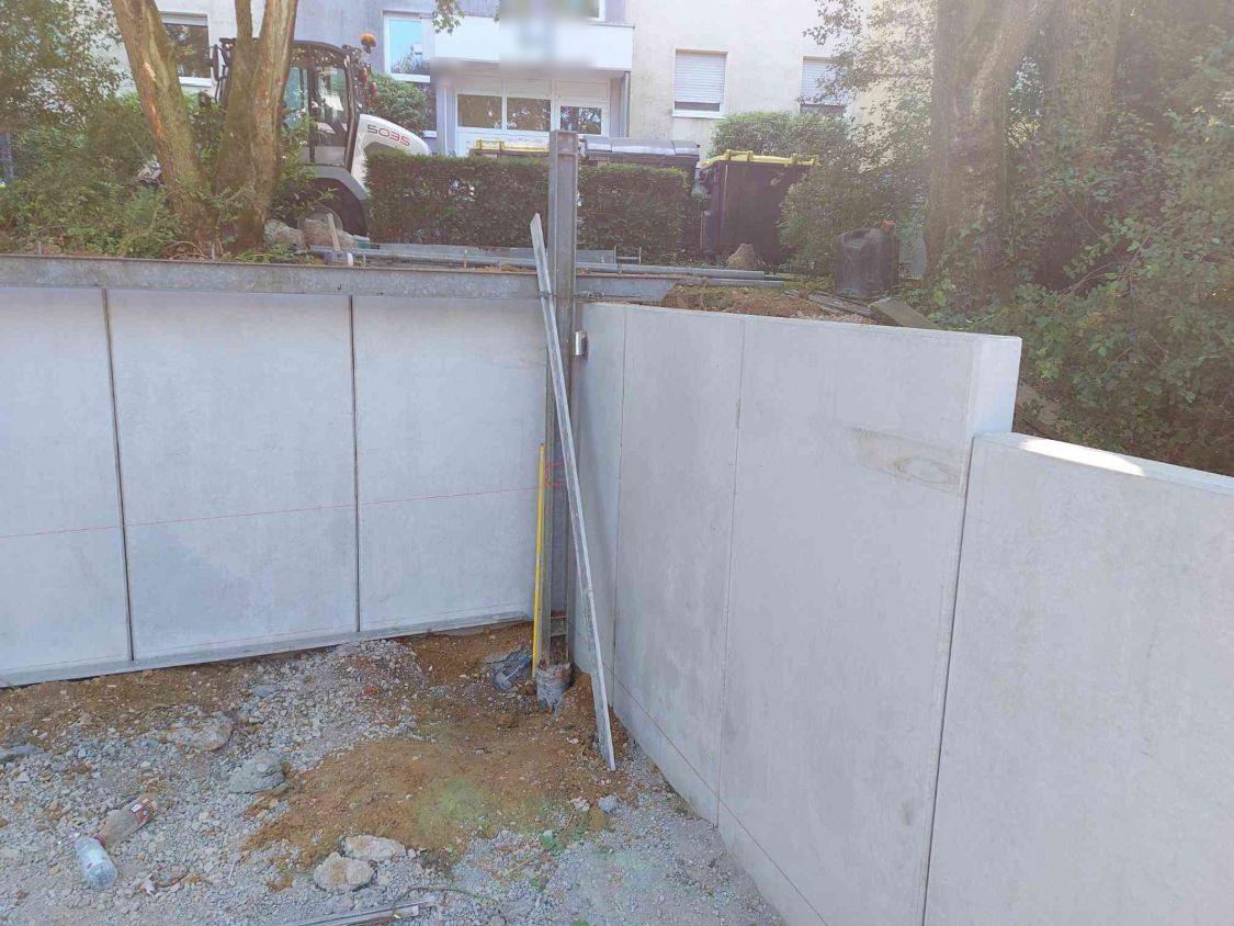 Ecke der Winkelstützmauer, dahinter der Hang mit Hecke und Wohnhaus