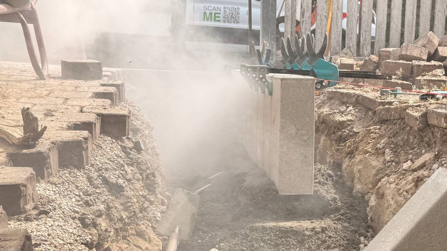 Betonpalisaden werden an der Schnur ausgerichtet und mit Zwingen in einer Reihe gehalten, daneben die alte Pflasterfläche