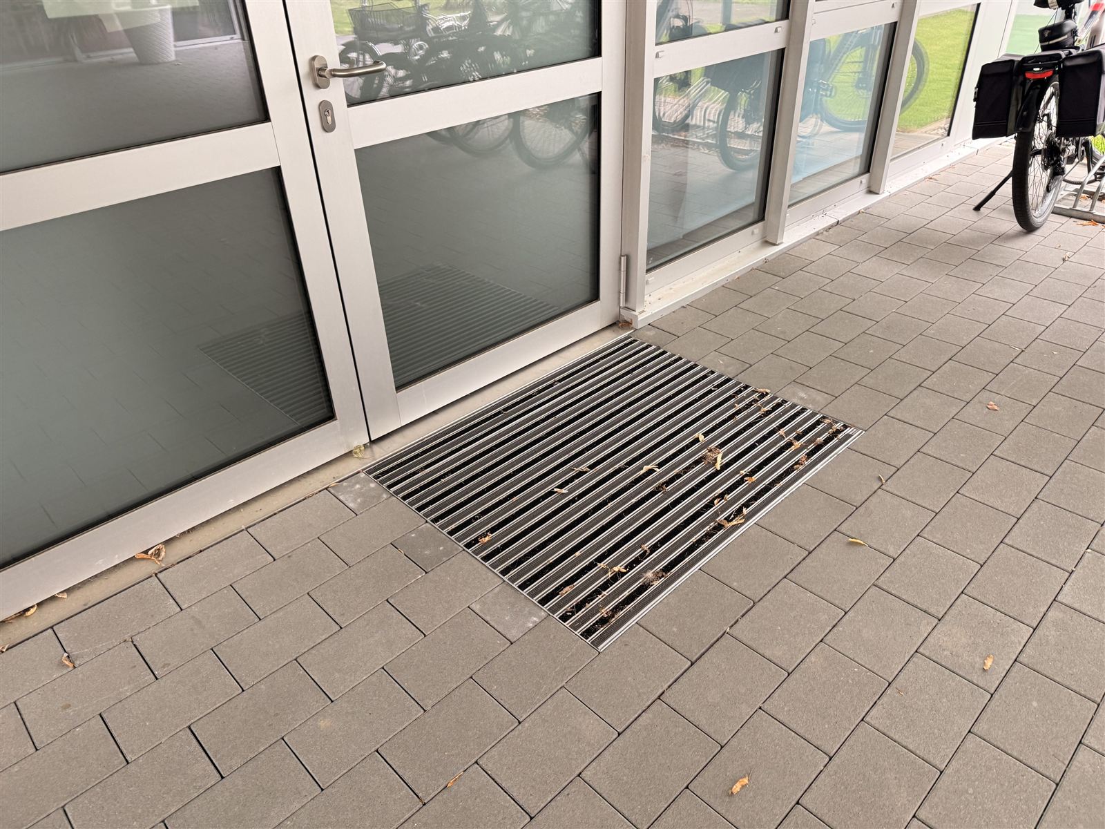 Pflaster vor einer Glastür mit eingelassenem Schmutzfangrost