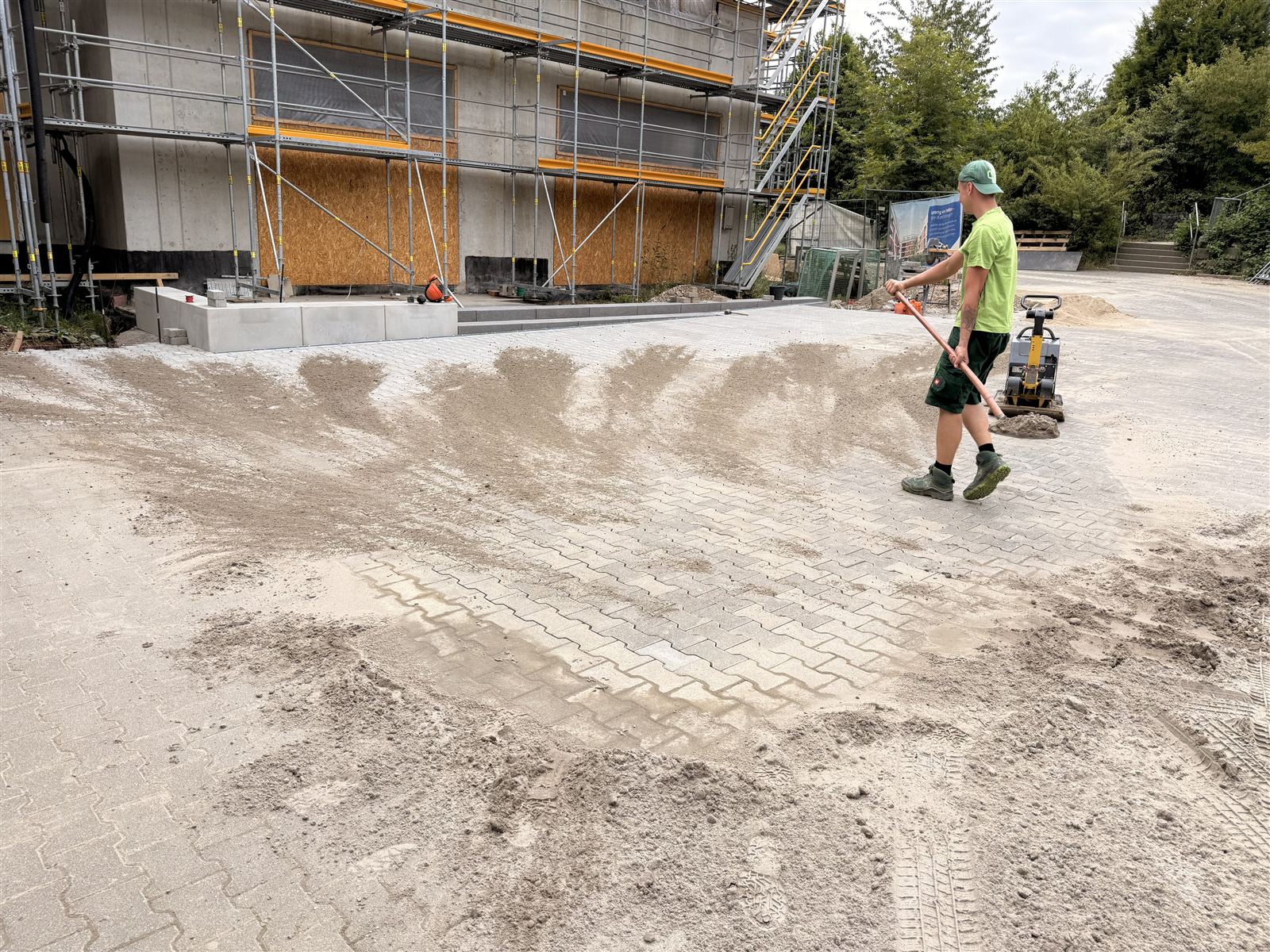 Mitarbeiter zieht das Planum für eine große Pflasterfläche ab, daneben die Rüttelplatte