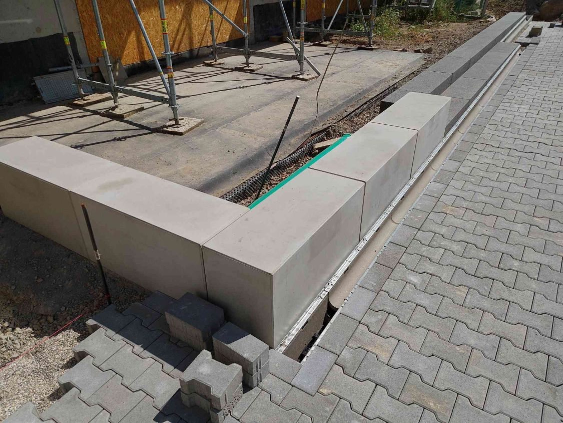Nachher: Ecke aus Sitzblöcken, davor die Rinne und das neue graue Verbundpflaster