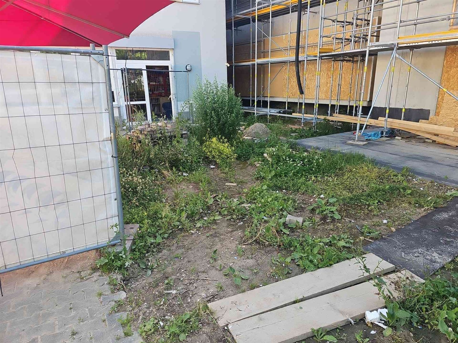 Vorher: verwilderte Fläche mit Gras, Unkraut und alten Platten vor dem eingerüsteten Anbau